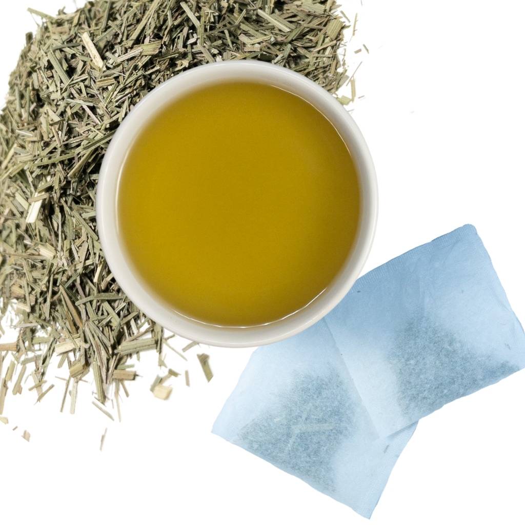 Brewed lemongrass leaf herbal tea with two tea bags and loose contents of tea bags in upper left hand corner