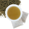 Brewed lemongrass leaf ginger root herbal tea with two tea bags and loose contents of tea bags in upper left hand corner