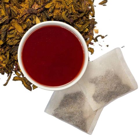 Brewed hibiscus turmeric herbal tea with two tea bags and loose contents of tea bags in upper left hand corner