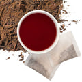 Brewed organic hibiscus cinnamon herbal tea with two tea bags and loose contents of tea bags in upper left hand corner