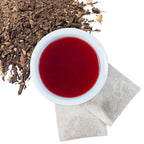 Brewed hibiscus ginger herbal tea with two tea bags and loose contents of tea bags in upper left hand corner