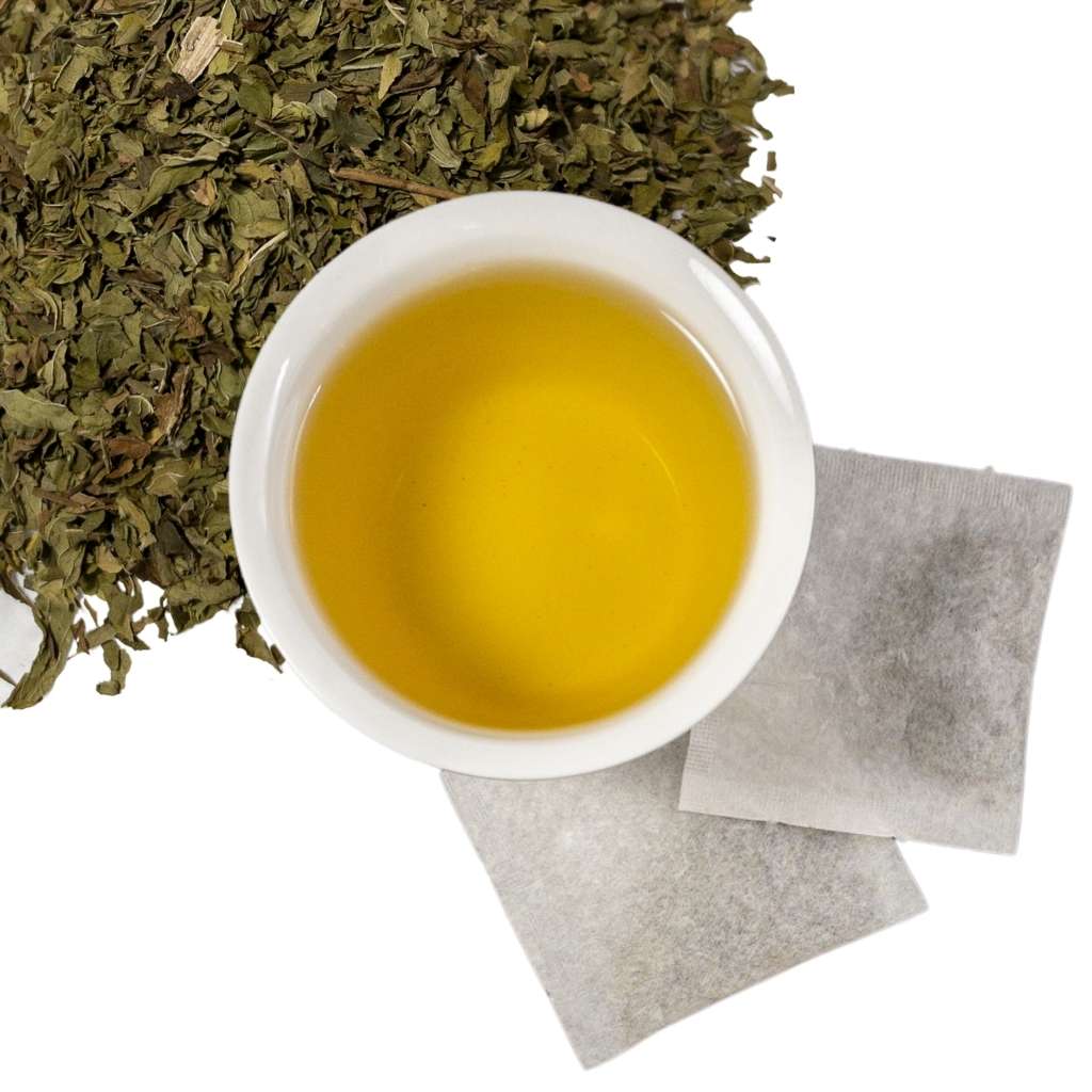 Brewed organic spearmint leaf herbal tea with two tea bags and loose contents of tea bags in upper left hand corner